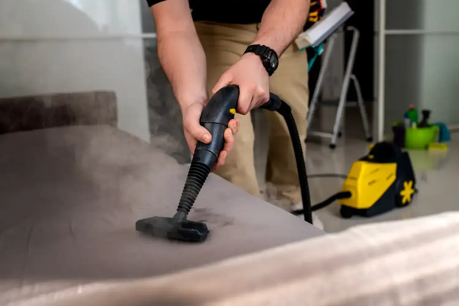Man steam cleaning a couch with a black and yellow steam cleaner.