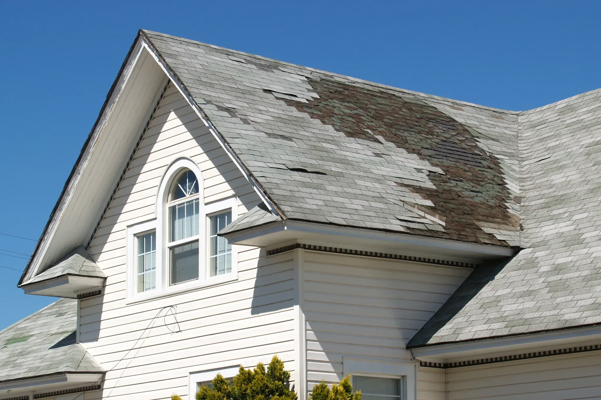 White house dormer with a window and damaged shingles on the roof.