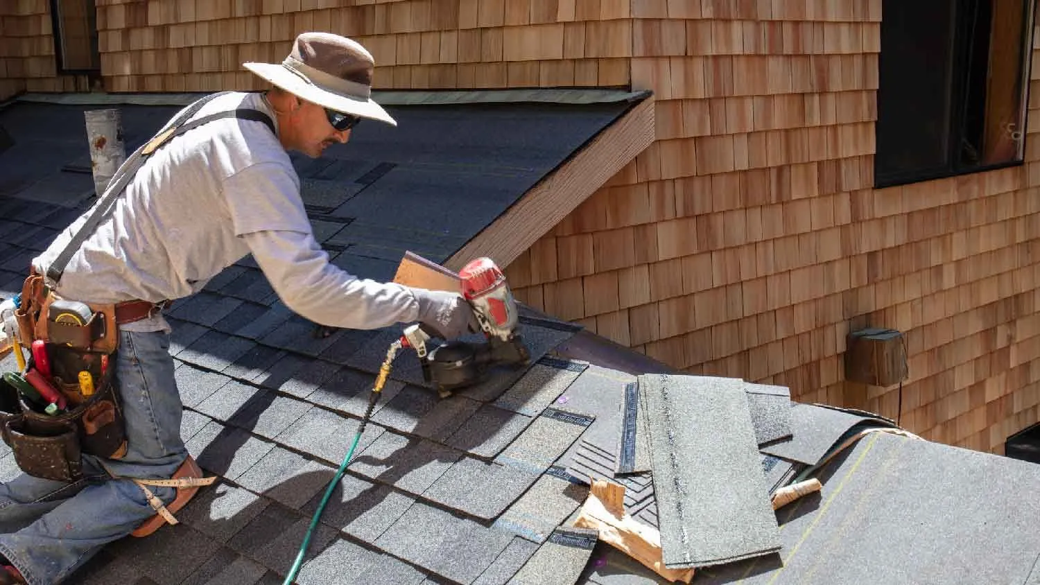 Roofer kneeling to inspect and work on the shingles at the edge of a home's roof.