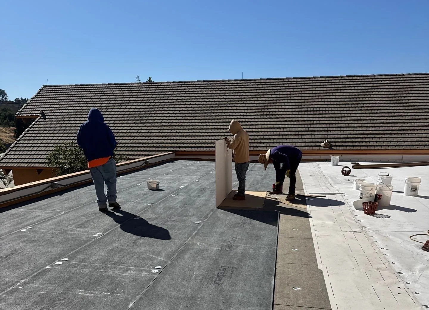 Crew working on a low-slope roof under a clear blue sky.